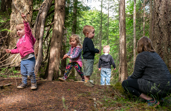 un groupe d’enfants joue dehors dans la forêt sous la surveillance d’une éducatrice
