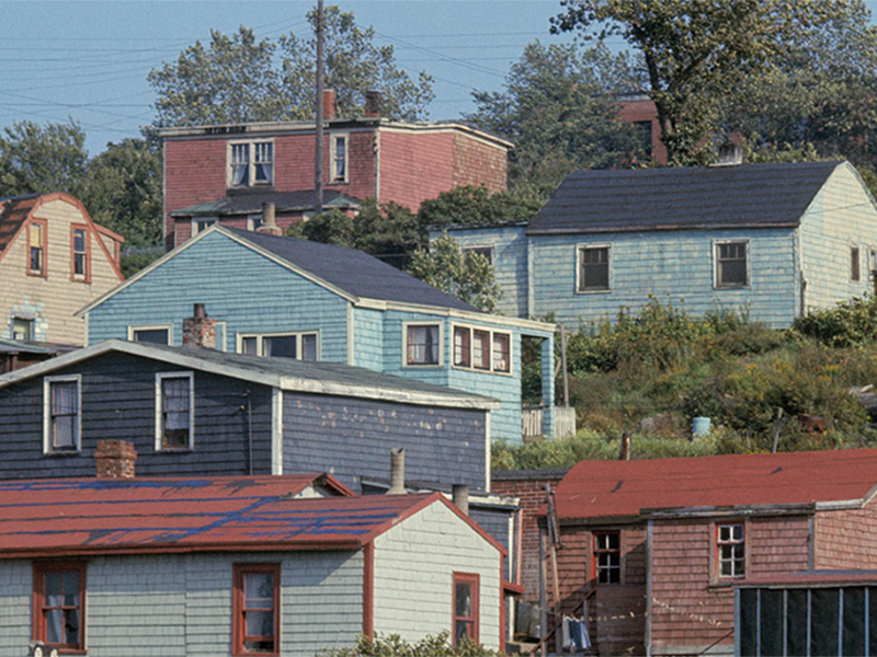 Image 1: Photo of several colourfully painted wooden houses on a slope.