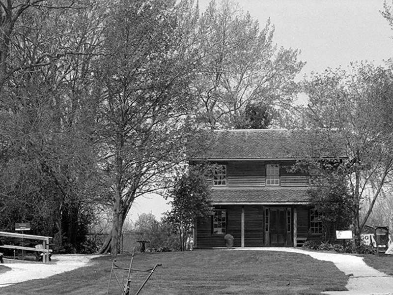 Image 4: Historical black and white photo of two wooden buildings with a lawn and path in front.