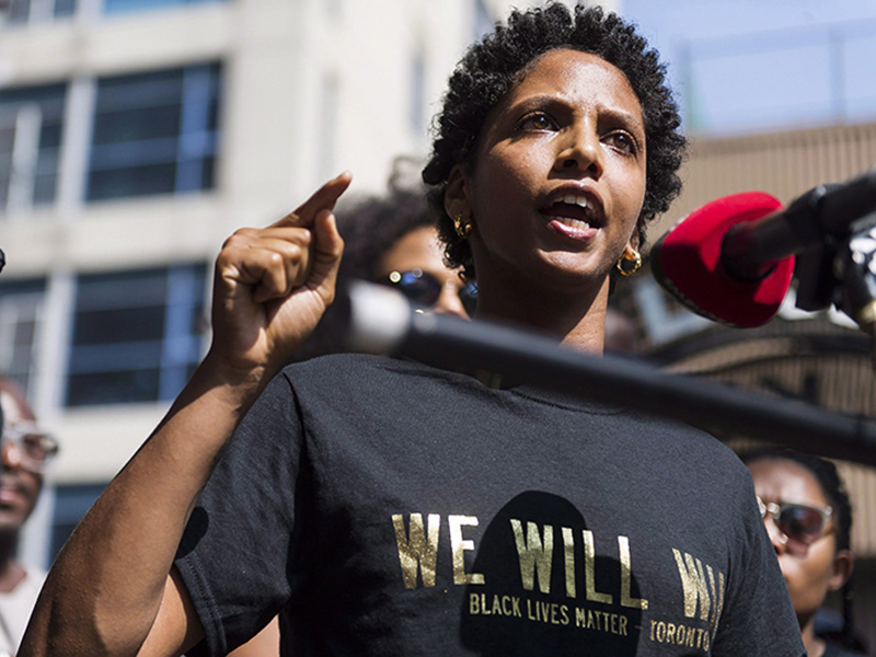 Image 7: Headshot of Janaya Khan at an activist rally with microphone in front of her.