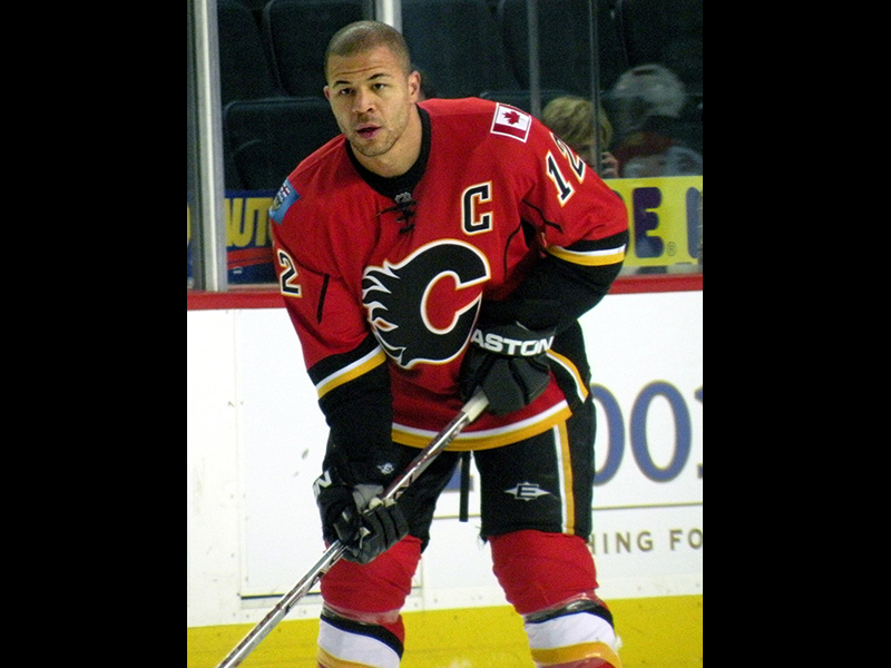 Image 6: Full body photo of Jarome Iginla on ice with Calgary Flames hockey uniform, holding hockey stick.