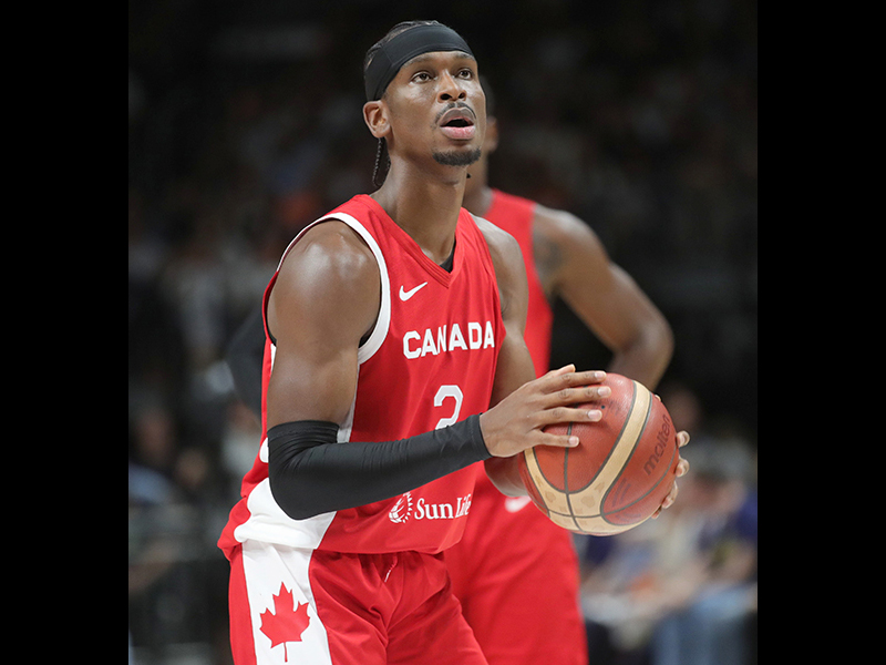 Image 1: Photo of Shai Gilgeous Alexander in a Team Canada basketball uniform, holding a basketball in both hands.